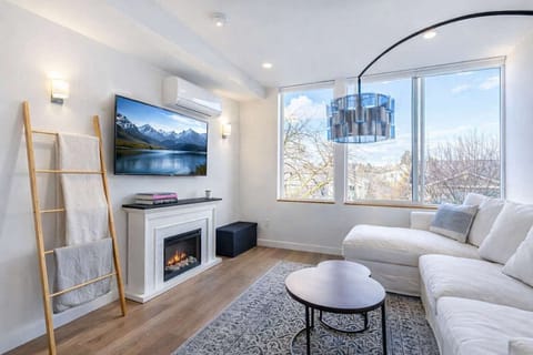 Airy modern living room with a cozy fireplace, plush sectional, chic lighting, and large windows showcasing calm mountain scenery.