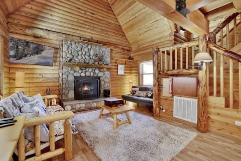 Cozy mountain living room with a stone fireplace, comfy seating, and smart TV—perfect for relaxing evenings, movie nights, and warm cabin vibes after outdoor adventures.