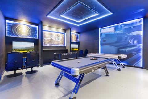 Experience the lively game room with a sleek air hockey table, promising endless fun. The modern design, accented by blue LED lighting and eye-catching wall art, sets a vibrant atmosphere ideal for gatherings and relaxation.