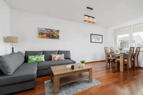A cozy living room with a gray sofa, a wooden coffee table, and a TV, complemented by warm wooden flooring and decorative pillows.

