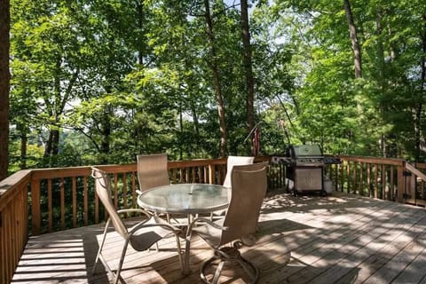 Spacious back deck w/ grill & patio seating, surrounded by trees for relaxed outdoor dining.