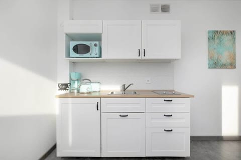 A compact yet fully equipped kitchen with sleek white cabinetry, a modern countertop, and pastel-colored kitchen appliances that enhance its stylish design.