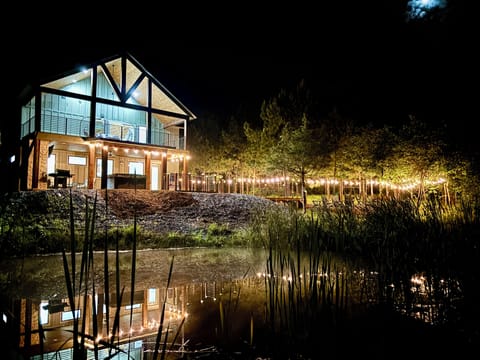 Cozy lakeside cabin glowing with string lights, reflecting on the water at night