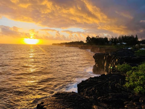 Breathtaking oceanfront view featuring dramatic lava rock cliffs, lush greenery, and a golden sunset over the water—perfect for serene coastal living or a tranquil getaway.