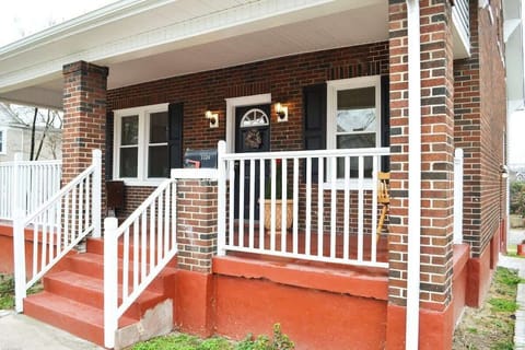 A picturesque red brick house with elegant white railings, a welcoming front porch adorned with black shutters, and a charming white door. Located downtown, this residence exudes classic charm in a prime location.