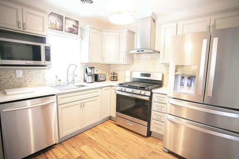 This kitchen exudes modern elegance, featuring pristine white cabinets and sleek stainless steel appliances. A warm wood flooring area hosts a stove, refrigerator, microwave, and dishwasher, creating a harmonious blend of contemporary style and functional