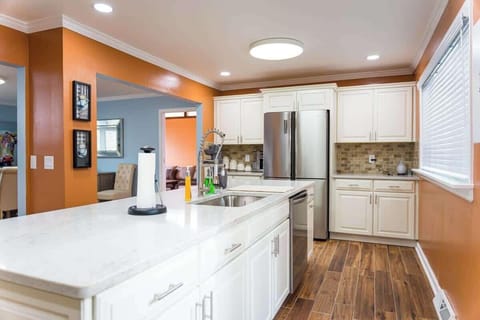 The image features a bright, contemporary kitchen with terracotta and light blue walls that create a warm contrast. White cabinetry and stainless steel appliances offer a clean, modern look.