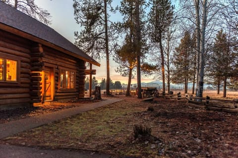 Log cabin lit up at dusk, with string lights on the porch and a warm glow through the windows