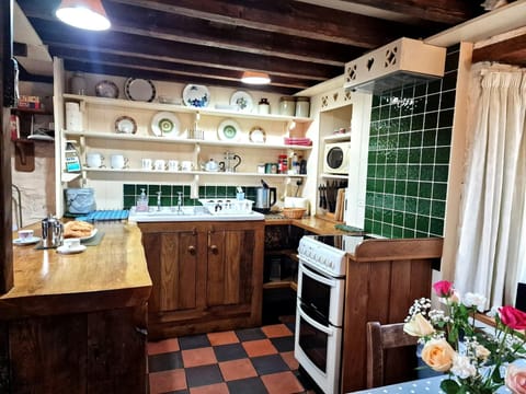 Kitchen with electric cooker, sink, shelving with crockery, kettle, microwave and toaster