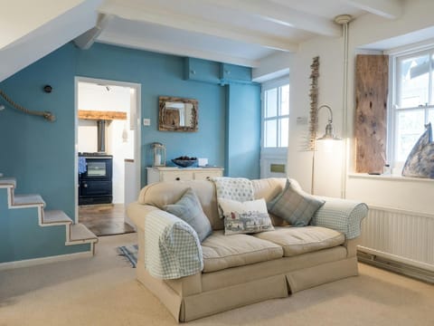 Living room with sofa, window with driftwood shutter, stairs to first floor