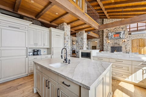 Kitchen island with farmhouse sink, marble counters, and stone fireplace in open floor plan.