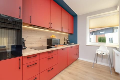 Modern kitchen with striking red cabinetry, wooden countertop, built-in appliances, and bright lighting.