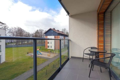 Sunny balcony with black table and two chairs, overlooking green courtyard and quiet surroundings.