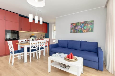 Cozy living room with blue sofa, white coffee table, dining area in background, and bright artwork on wall. 