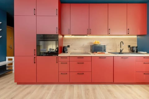 Modern kitchen with striking red cabinetry, wooden countertop, built-in appliances, and bright lighting.