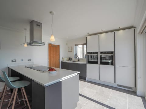 Kitchen with breakfast bar, hob and cooker hood, ovens and sink