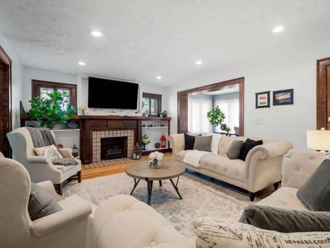 Relax in this bright living room featuring tufted sofas, a stylish coffee table, hardwood floors under a plush area rug, and a classic wood-burning fireplace—perfect for cozy evenings or social gatherings! ️️