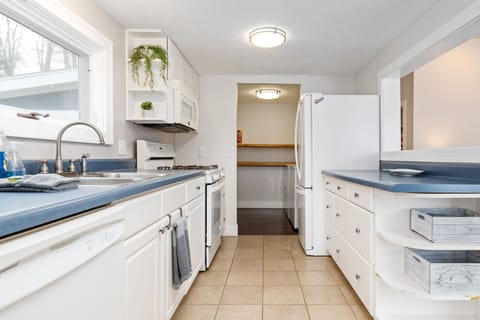 Our kitchen radiates a bright and sophisticated charm with its white cabinetry and blue countertops, complemented by the warm natural light streaming through the windows. The space is a perfect blend of elegance and functionality.