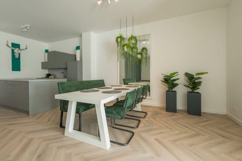 Dining area with a modern white table, green chairs, and hanging plants adding a vibrant, natural atmosphere.