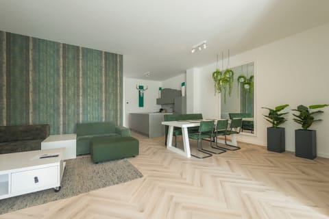 Spacious living area with green modular seating, a white coffee table, and a modern dining setup, complemented by vibrant accent wallpaper and decorative plants.