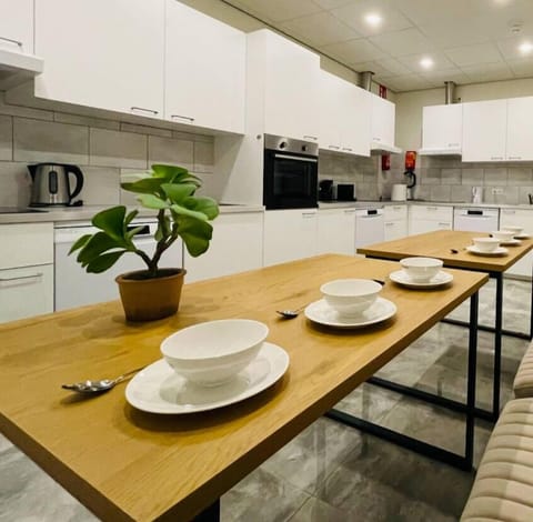 This shared kitchen is available to all guests. It features a spacious and well-lit area with modern appliances, a long dining table, and comfortable seating, perfect for communal meals and socializing.
