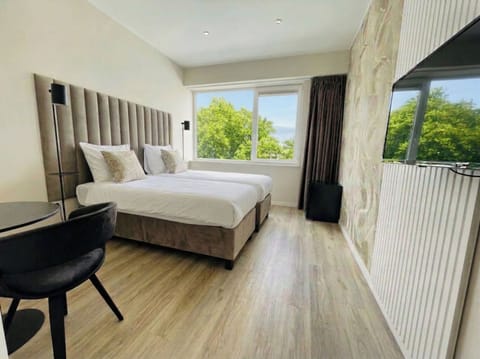 Bright modern bedroom with twin beds, large window view of greenery, wooden floor, wall-mounted TV and soft neutral tones for a calm, clean stay.