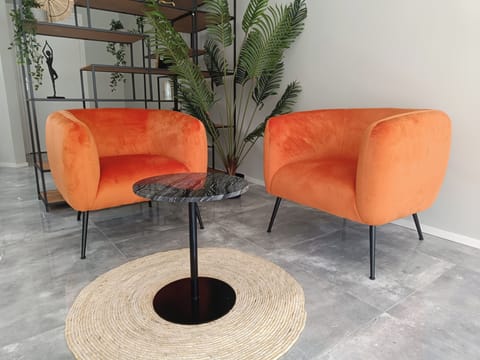 Vibrant orange chairs with a sleek black table, set against lush greenery, perfect for a cozy and stylish seating experience.