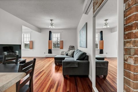 Bright living room with rich hardwood floors, exposed brick accents, and large windows looking onto the street.
