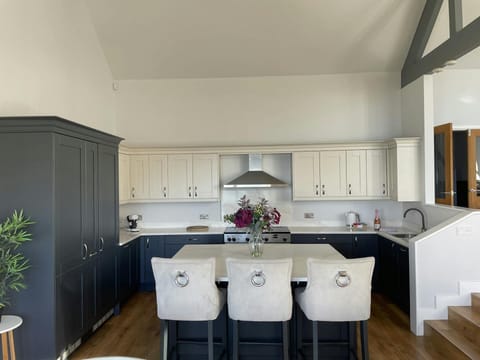 Open plan kitchen with breakfast bar island with three bar stools and fresh flowers in vase