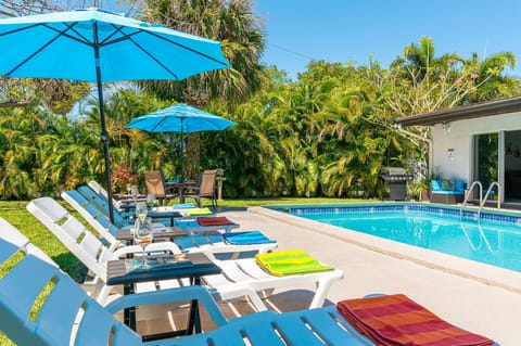 Welcome to your own private oasis, where an expansive resort-style pool awaits, flanked by sun loungers beneath umbrellas on a meticulously manicured lawn.