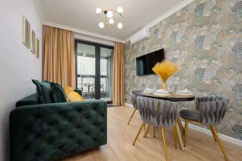 A stylish dining area with a round glass table, elegant blue chairs, and a luxurious green velvet sofa against a patterned accent wall.

