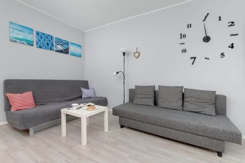 A cozy living area with a gray sofa, wall-mounted clock, and a modern coffee table, accented by minimalist decor.

