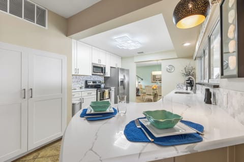 - Enjoy casual bites or drinks at this sleek bar with marble inspired counters
- Modern pendant lighting adds a warm glow to this bright open kitchen space
- Stylish place settings and custom cabinetry offer a clean coastal vibe