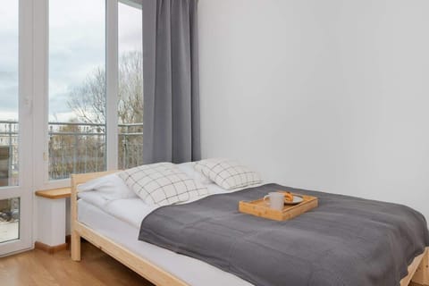 Bright bedroom with a double bed, wooden desk and large window with sheer curtains.