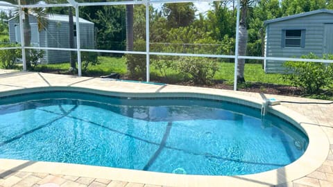 Beautiful, screened-in heated pool featuring chic lounge chairs and a BBQ area.