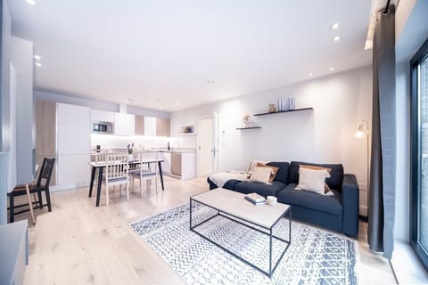 Open-plan living room with a fully equipped kitchen, sofa bed suitable for the 5th and 6th guests,  a dedicated desk with a 27-inch monitor, and a smart TV.