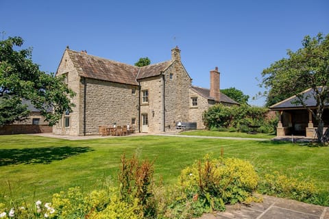 Hollins Farmhouse holiday home in the Yorkshire Dales with a traditional stone exterior, large lawn, hot tub and outdoor seating.