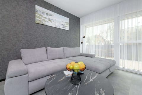 A stylish living room featuring a soft grey sectional sofa, modern finishes, and large sheer curtains that fill the space with daylight.