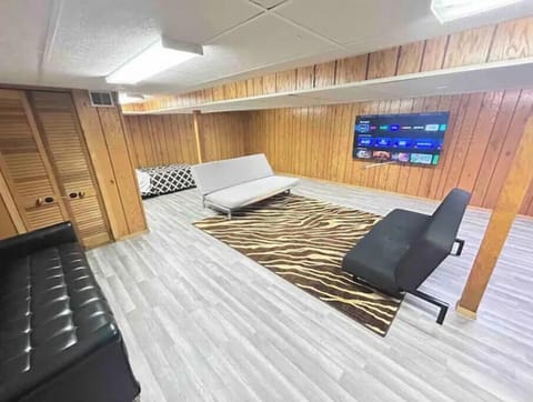 Basement TV room with futons, games, 75" smart TV, and work desk.