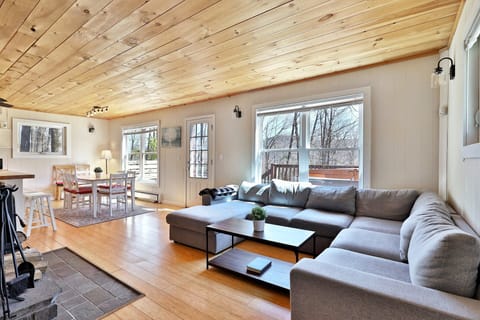Cozy living room on the main floor, featuring a smart TV and a wood-burning fireplace in front the large U-shaped sofa. At the back, the dining area with seating for six, and additional space at the counter next to it.