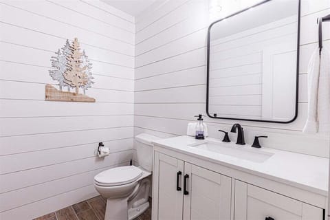 A clean, modern bathroom with white cabinetry, a large mirror, and farmhouse-style accents in a professionally managed Bryson City cabin.