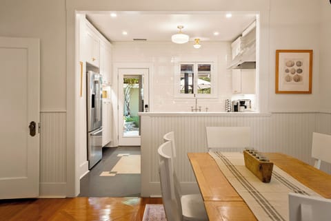 This charming home features a functional gourmet kitchen that seamlessly connects to the formal dining area, offering a sleek stainless steel refrigerator and custom white cabinetry with gold hardware.