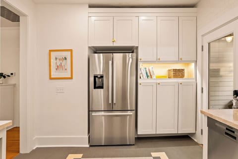 This charming kitchen boasts high-end storage and organisation, having a floor-to-ceiling custom pantry and a stainless steel French-door refrigerator. It is beautifully finished with white shaker-style cabinetry and a warmly lit display nook for cookbooks