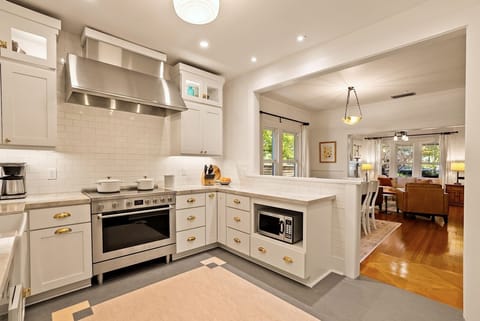 This designer chef's kitchen offers custom white cabinetry with gold hardware, a professional-grade stainless steel range with a matching high-capacity vent hood, and a classic white subway tile backsplash.