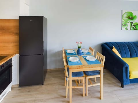 Wooden dining table and chairs standing next to the functionally equipped kitchenette with such appliances as kettle, oven, and fridge with freezer.