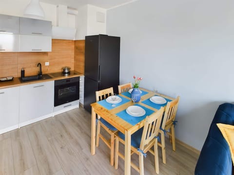 Dining area with wooden table and chairs for four people situated next to the kitchenette with fridge and freezer, oven, kettle, induction hob and dishwasher.