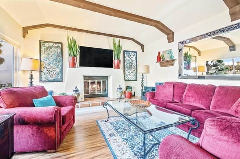 Vibrant living room with rustic wooden beams, cozy fireplace, bold red seating, elegant glass coffee table, decorative blue accents, large mirror, warm lighting, and stylish decor creating a welcoming atmosphere.