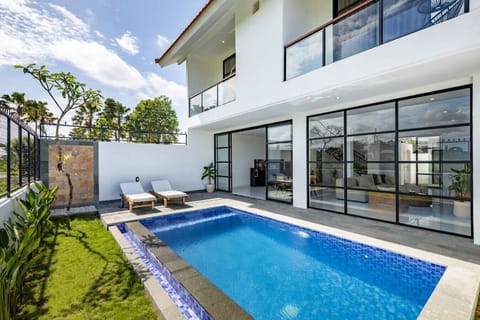 our modern villa with a sparkling private pool, loungers ready for sunbathing, and expansive glass doors that open to a chic, comfortably furnished living area.