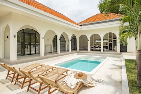 a luxurious white villa with a refreshing pool, surrounded by tropical plants, offering a serene and inviting outdoor living space.