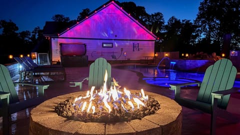 Outdoor fire pit and pool area illuminated with colorful lighting for a relaxing evening.